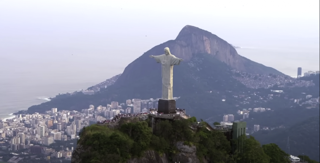 Huge white statue with arms wide open, positioned at the mountaintop, overlooking the cityscape