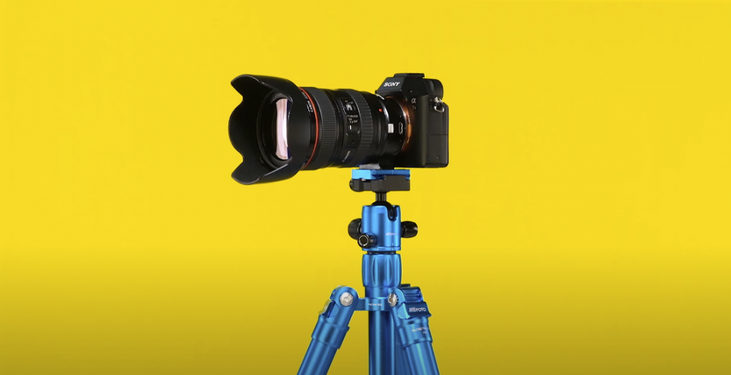 Photo of a camera placed in a blue MeFOTO Backpacker Air tripod, against a yellow background