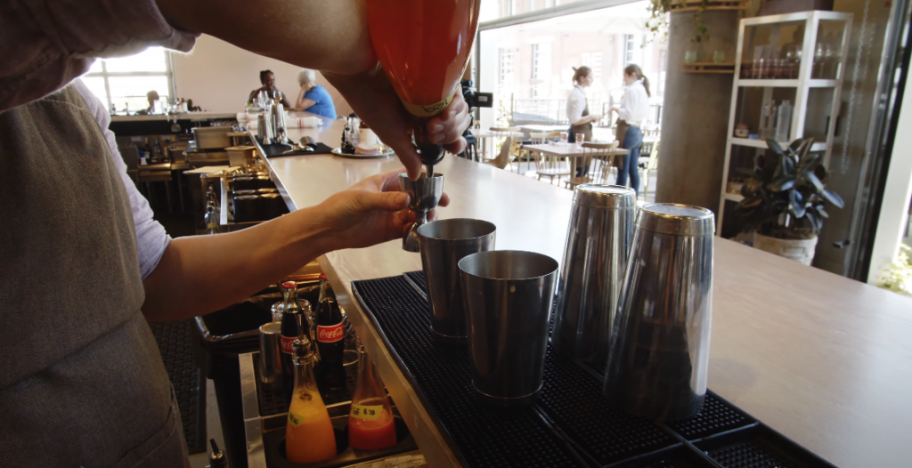 Photo of someone preparing a drink inside the restaurant, with the dining area visible in the background