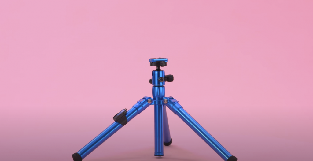 Photo of a blue MeFOTO Backpacker Air tripod with its legs spread out, against a pink background