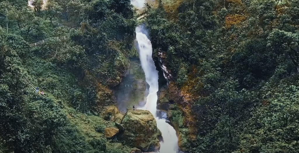 Photo of a narrow waterfall framed by dense trees and lush green surroundings