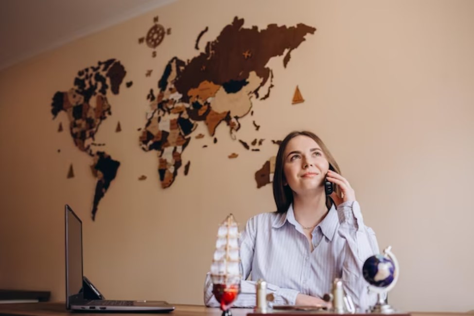 a beautiful travel agent talking on the phone while sitting at the table in the office with a map on the wall