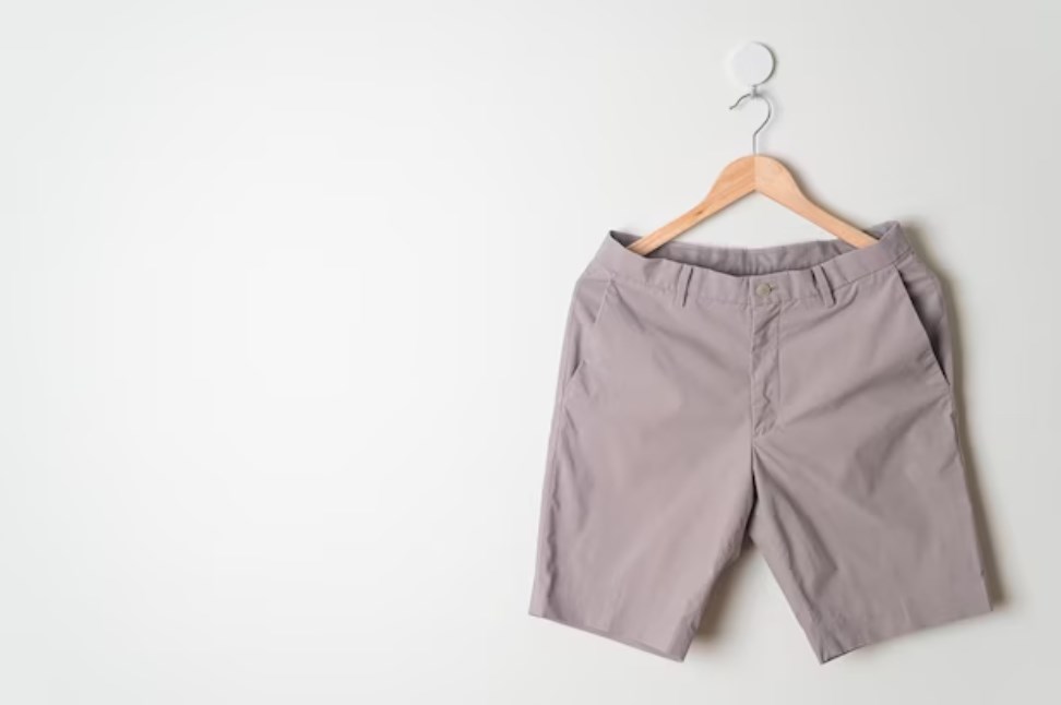 beige short-pants hanging on a wood hanger against a wall