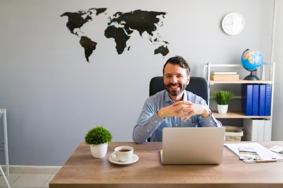 a portrait of a male travel agent smiling and making eye contact while sitting at the table in the office